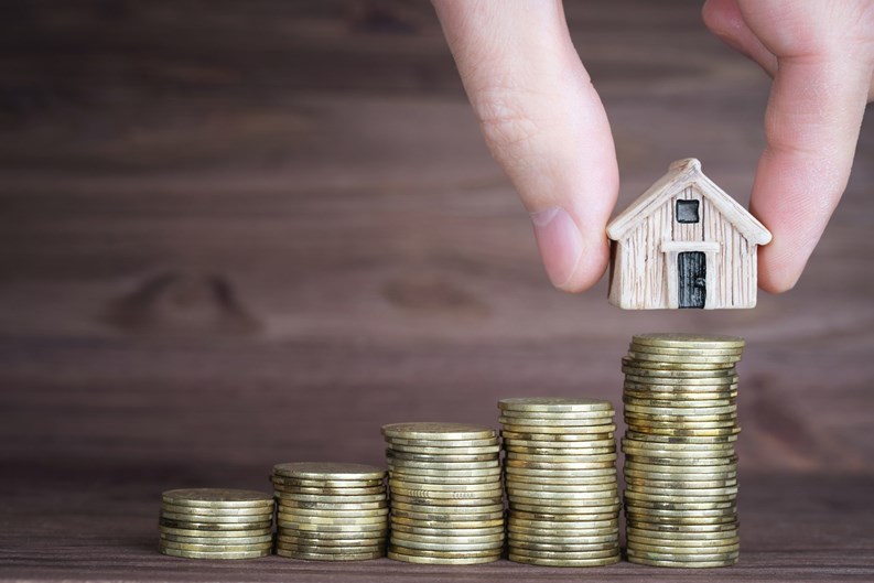 Placing a miniature houses on top of a coins stack against a wooden background. Building a step by step mortgage plan